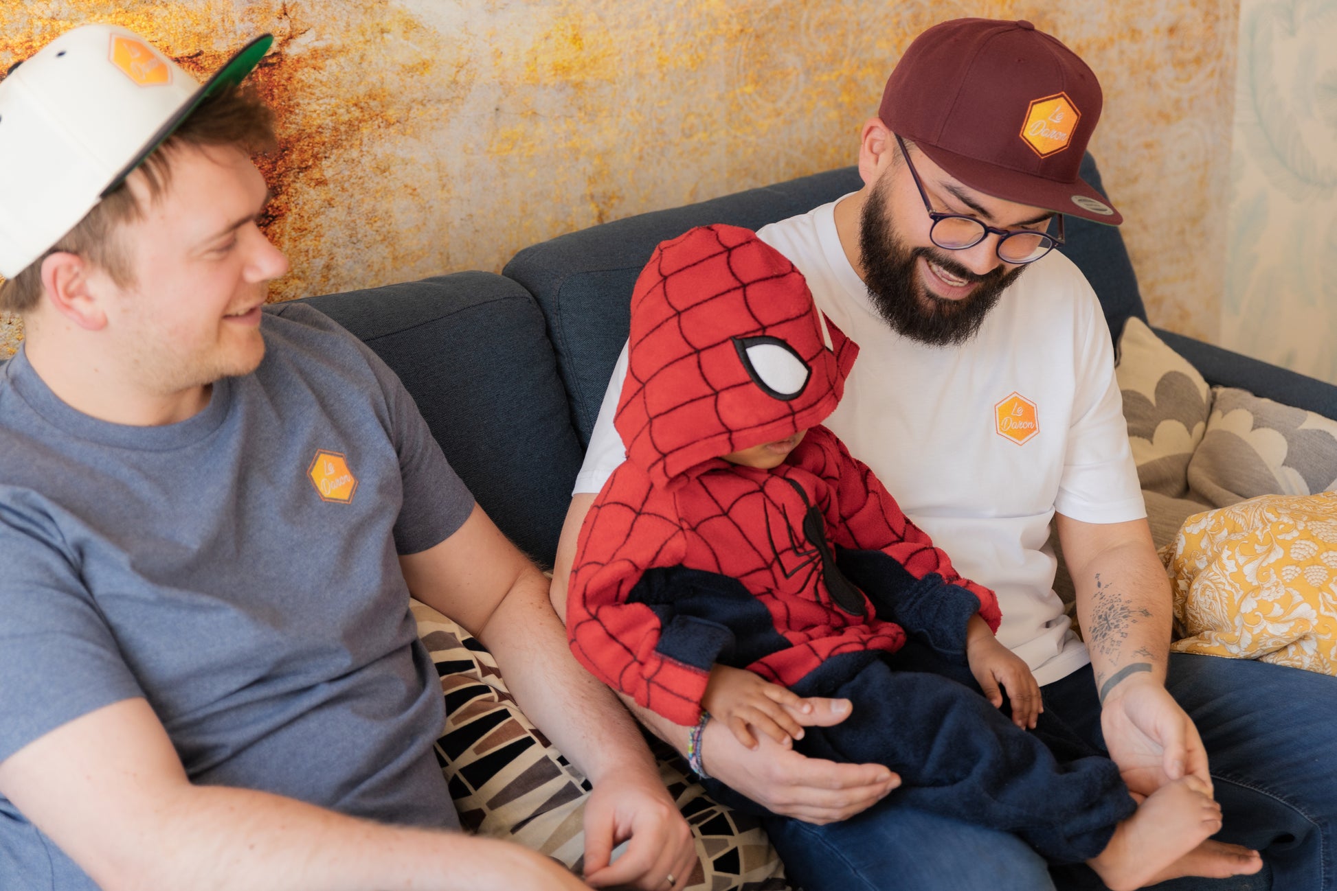Casquette Le Daron brodée - coloris bordeaux et crème - portée par deux papas avec Spiderman bébé au milieu