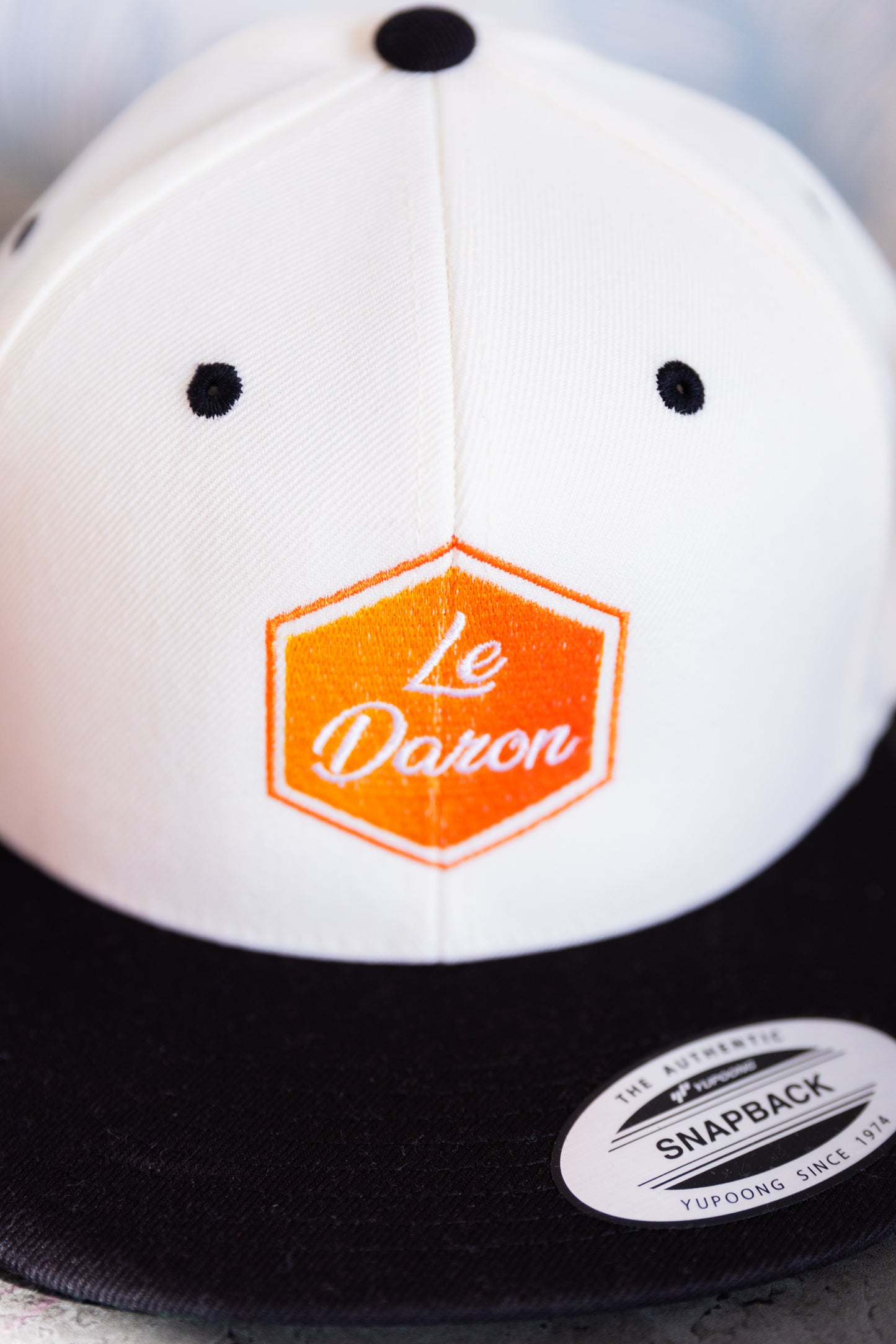 Casquette Le Daron brodée - détail du logo hexagonal orange - vue rapprochée, posée à plat