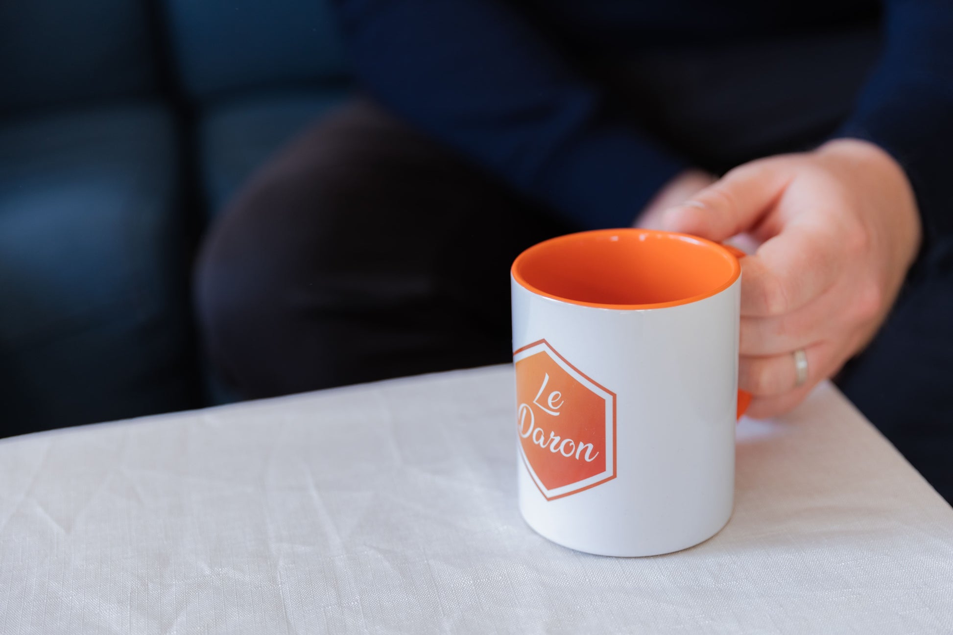 Mug Le Daron blanc - logo orange brodé - posé sur une table de salon